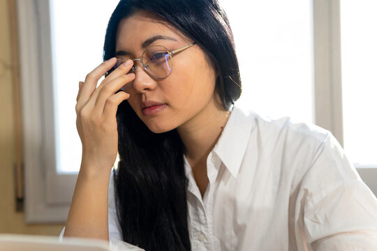 Crop thoughtful ethnic female self employed freelancer in eyeglasses working on gadget at home
