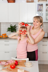 Mom and daughter cook in the kitchen. A young woman cooks with her child in the kitchen at home. Girls in pink clothes cook pizza. Happy and cheerful mom and daughter