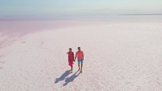 Aerial epic drone image of lovely romantic couple walking along bright colorful pink water of mineral lake with white salty coast. panoramic view. Concept inner tourism in unusual places in Ukraine