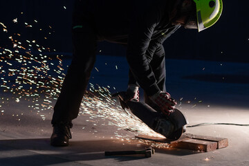 Unrecognizable male welder in protective helmet and goggles cutting iron details with chop saw during work at industrial factory at night