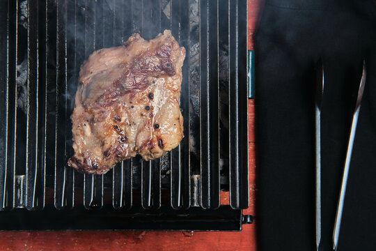 Pieces of raw beef meat preparing on hot metal grill in kitchen of restaurant