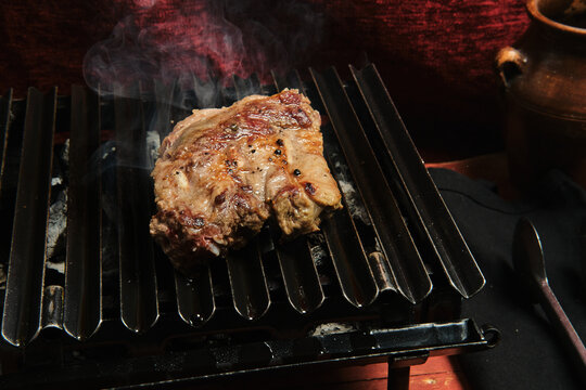 Pieces of raw beef meat preparing on hot metal grill in kitchen of restaurant