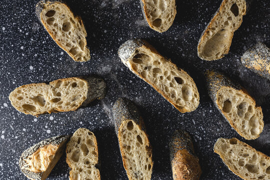 From above of appetizing crusty bread near wheat spikes and dark fabric on table