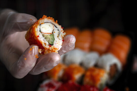 Crop unrecognizable chef in gloves showing platter with set of palatable assorted sushi in dark room