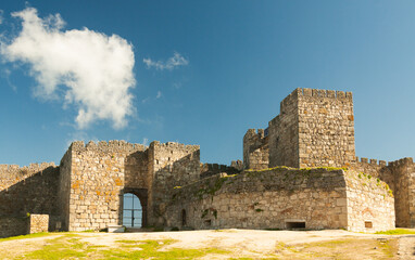 Towers and stone walls facade with merlons on a cloudy day at the Castle of Trujillo.