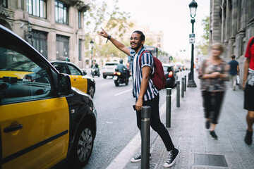 Smiling ethnic man hailing taxi on street