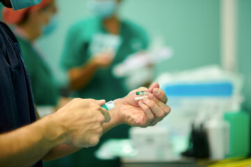 Side view of crop unrecognizable male doctor in medical uniform and mask filling syringe with medicine while preparing for operation in hospital