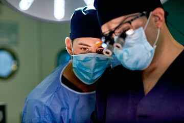 Unrecognizable young attentive male practitioner in sterile gown and mask following operation process performing by professional doctor in modern clinic
