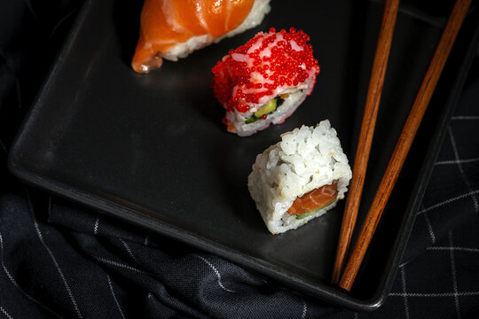 Top view composition of delicious fresh various sushi and bamboo chopsticks served on black platter on checkered cloth