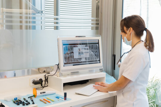Side view competent female dentist in uniform examining x ray picture on screen in light modern dental clinic