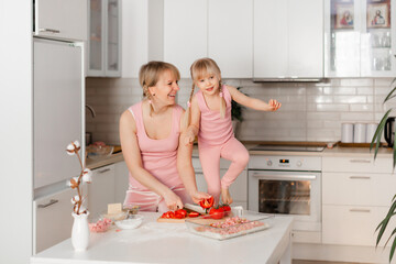 Mom and daughter cook in the kitchen. A young woman cooks with her child in the kitchen at home. Girls in pink clothes cook pizza. Happy and cheerful mom and daughter