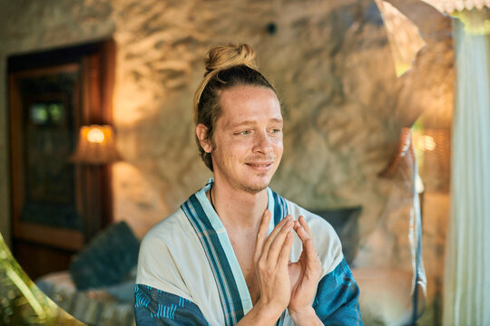 Young male with Namaste hands looking old building while practicing yoga in summer