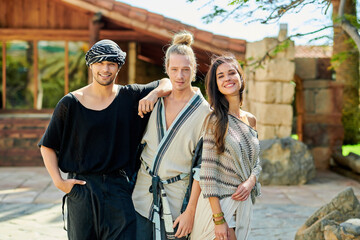 Happy multiracial partners looking at camera during summer vacation against old house in back lit
