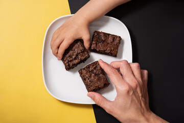Hands picking pieces of fresh brownie on black and yellow background