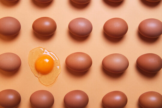 From above of pattern of whole brown eggs placed in even rows with raw eggs on peach table in studio