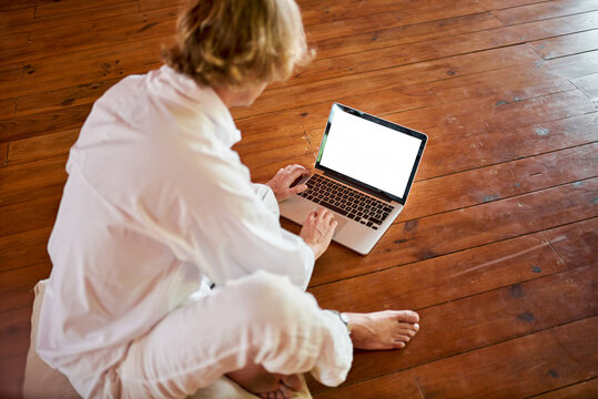Young concentrated male sitting with crossed legs browsing on netbook in meditation room while practicing yoga