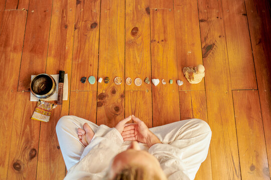 From above of crop unrecognizable barefoot male practicing yoga on floor near bowl gong and Buddha statuette