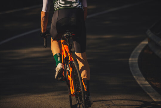 Back view of young sportsman in activewear and helmet riding bicycle on asphalt road amidst lush green trees on sunny day