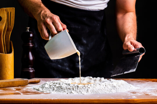 Crop man with scraper pouring egg mix into pile of wheat flour making bread in bakery