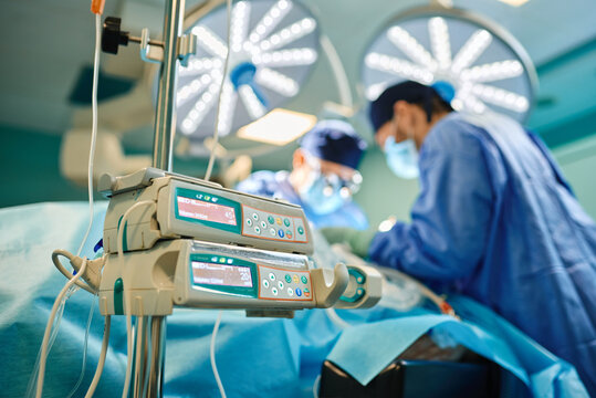 From Below Of Modern Infusion Pump Placed In Operating Room Near Unrecognizable Male Doctors Performing Surgery In Contemporary Hospital