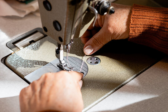 High angle of crop faceless senior seamstress putting thread into sewing machine in workshop