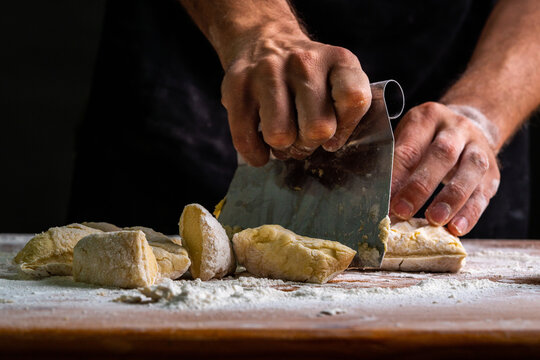 From above of man dividing raw bread dough with scraper on wooden table in baker