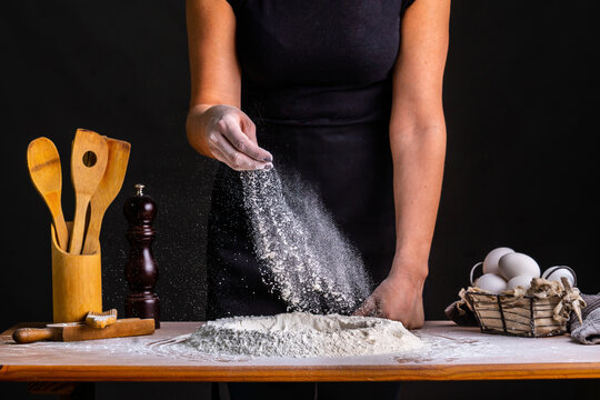 Faceless cropped person baker sprinkling flour while making bread dough with wheat flour and eggs at table