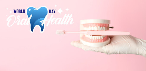 Hand of dentist with model of jaw and toothbrush on color background. World Oral Health Day