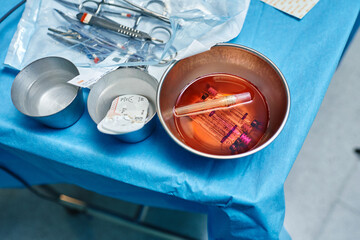 From above of syringes in bowl with bloody water placed on sterile field near various surgical instruments in operating theater