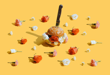 still life of a burger on a yellow background. flowers instead of meat in a burger. the burger will be pierced with a knife. burger with flower buds