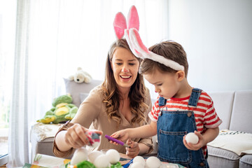 Obraz na płótnie Canvas Mother and son painting Easter eggs. Preparing for Easter. Mother and son paint eggs. Family at home. Happy family preparing for Easter. Cute little child wearing bunny ears on Easter day