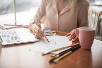 Young woman designer in cafe sitting drawing sketch of dress close-up