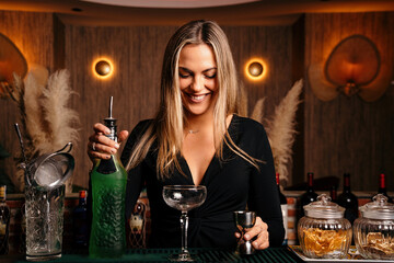 Alluring young female bartender with long blond hair preparing alcohol drink cocktail at counter