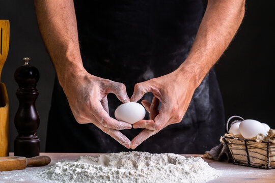 Faceless baker making heart shape hand while holding raw chicken egg into sifted flour pile on table cooking bread