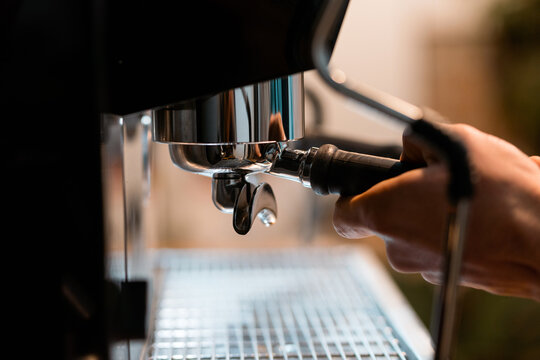 Crop anonymous barista using portafilter in coffee machine while preparing drink in cafe