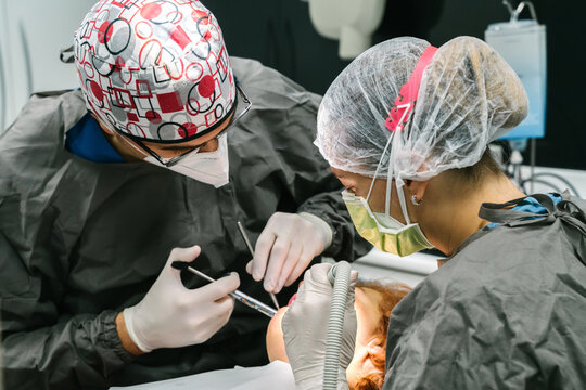 Professional dentist applying anesthetic injection to patient while working with assistant in modern stomatology clinic