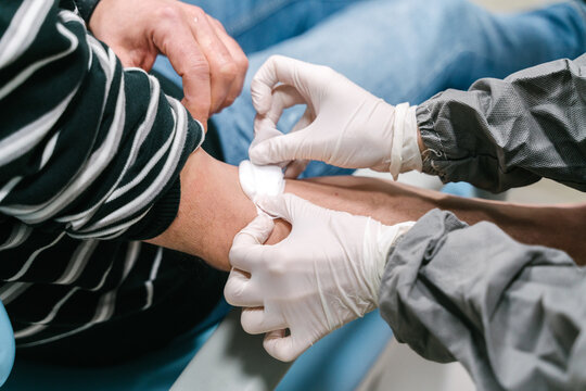 High angle side view of crop anonymous nurse in latex gloves applying patch on arm of patient after performing blood test in clinic