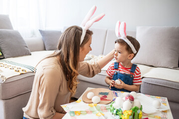 Having fun during Easter preparation. Portrait of pretty young mother hugging little boy while celebrating Easter at home, copy space. Mother and son painting easter eggs