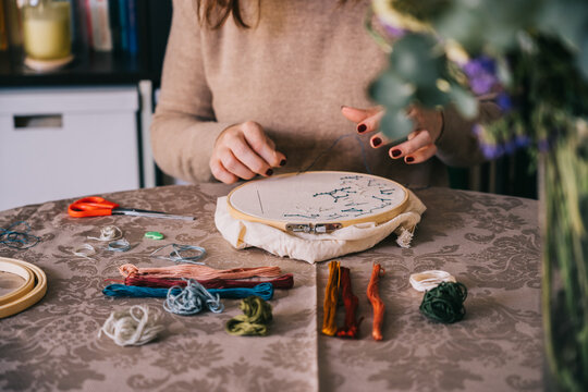 Front view of crop female with hoop and threads embroidering star constellations while sitting at table in light workshop
