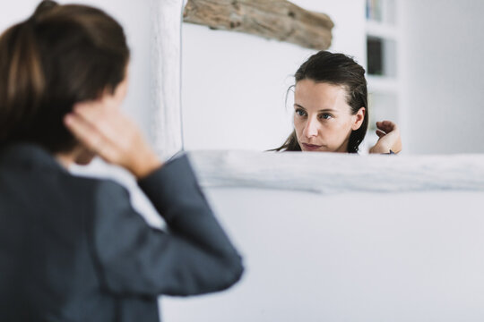 Young Female In Formal Outfit Looking At Mirror And Adjusting Hair While Preparing For Workday In Morning