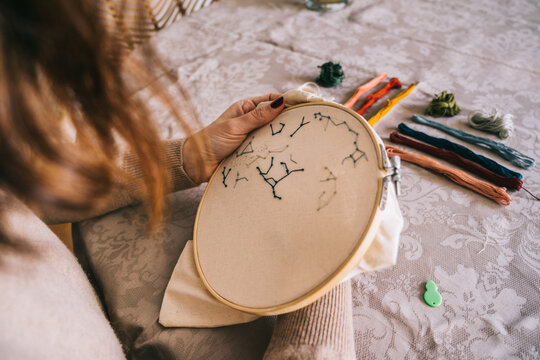 From above crop female with hoop and threads embroidering star constellations while sitting at table in light workshop