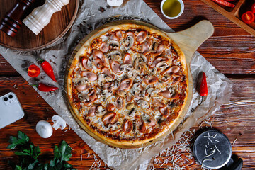 The pizza is on the kitchen table with the ingredients scattered around. Pizza with sausages