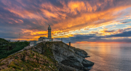 Scenic view of small island with lighthouse called Faro de Cabo Mayor connected with coastline by bridge under dramatic cloudy sky at sunset time in Santander in Spain