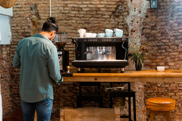 Back view male barista using portafilter and preparing coffee in modern coffeemaker while standing at counter in cafe