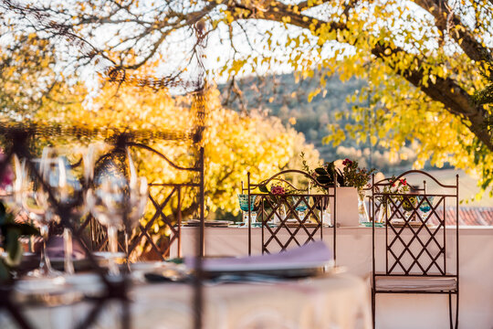 Spacious veranda with plates wineglasses and cutlery placed on tables decorated with fresh flowers for wedding celebration