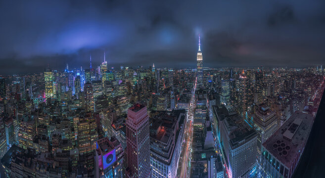 From above aerial cityscape of New York city with glowing towers and illuminated streets under cloudy night sky