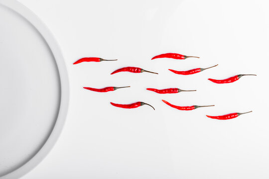 High angle composition of hot red chili peppers arranged near plate against white background