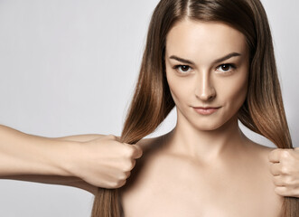 Portrait of young beautiful woman with silky long straight hair looking at camera and holding her...