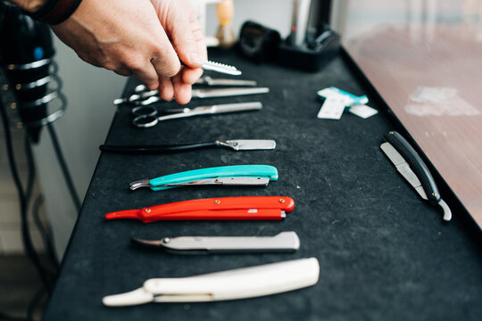 Crop anonymous beauty master with collection of razors and manual instruments at table in hairdressing salon