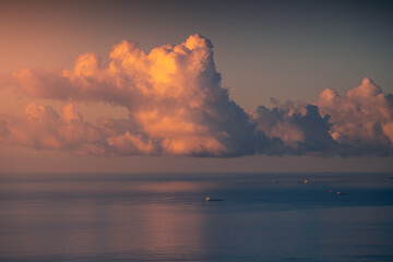 Boats floating in calm sea under sky with clouds illuminated by sunset sun in Cadiz